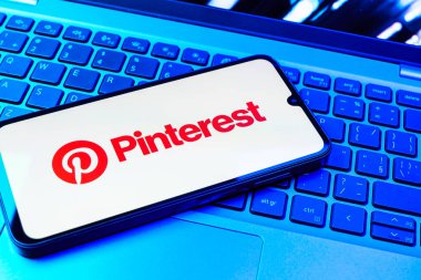 Prag, Çek Cumhuriyeti - 08 01 2025: Dizüstü bilgisayarın üzerinde duran bir cep telefonu Pinterest logosunu gösteriyor. Pinterest fikirleri görsel olarak keşfetmek ve kaydetmek için bir platformdur..