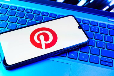 Prag, Çek Cumhuriyeti - 08 01 2025: Dizüstü bilgisayarın üzerinde duran bir cep telefonu Pinterest logosunu gösteriyor. Pinterest fikirleri görsel olarak keşfetmek ve kaydetmek için bir platformdur..