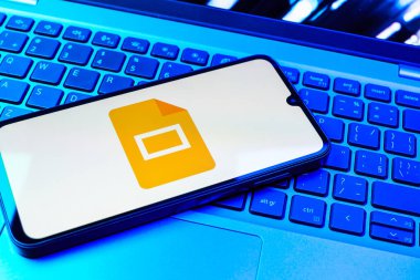 Prag, Çek Cumhuriyeti - 08 01 2025: Laptop klavyesinde duran bir cep telefonu Google Slides logosunu görüntüler. Google Slides sunumlar ve slayt gösterileri oluşturmak için bir platformdur.