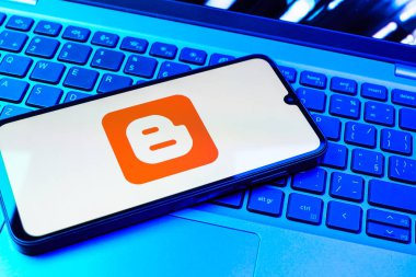 Prag, Çek Cumhuriyeti - 08 01 2025: Dizüstü bilgisayarın üzerinde duran bir cep telefonu Blogger logosunu gösterir. Blogger blog oluşturma ve yayınlama için bir platformdur.