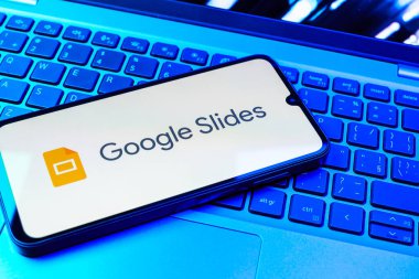 Prag, Çek Cumhuriyeti - 08 01 2025: Laptop klavyesinde duran bir cep telefonu Google Slides logosunu görüntüler. Google Slides sunumlar ve slayt gösterileri oluşturmak için bir platformdur.