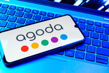 Prag, Çek Cumhuriyeti - 08 01 2025: Dizüstü bilgisayarın üzerinde duran bir cep telefonu Agoda logosunu gösteriyor. Agoda, otelleri ve seyahat yerlerini ayırtmak için bir platform..