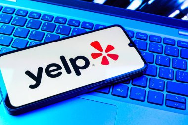 Prag, Çek Cumhuriyeti - 08 01 2025: Laptop klavyesinde duran bir cep telefonu Yelp logosunu gösterir. Yelp yerel işletmeleri bulmak ve incelemek için bir platformdur.