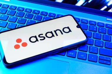 Prag, Çek Cumhuriyeti - 08 01 2025: Dizüstü bilgisayarın üzerinde duran bir cep telefonu Asana logosunu gösterir. Asana görev yönetimi ve takım işbirliği için bir platformdur..