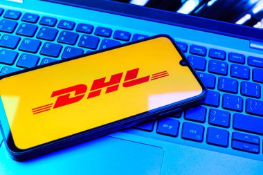 Prag, Çek Cumhuriyeti - 08 01 2025: Dizüstü bilgisayarın üzerinde duran bir cep telefonu DHL logosunu gösterir. DHL uluslararası nakliye hizmeti sunan bir lojistik şirketidir..
