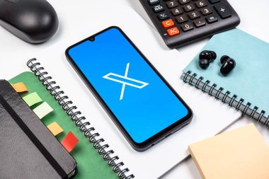 Prag, Çek Cumhuriyeti - 08 18 2025: Merkezinde X logosu sergilenen bir cep telefonu ile ofis malzemeleri düzenlemesi. X, kısa gönderileri ve güncellemeleri paylaşmak için bir platformdur.