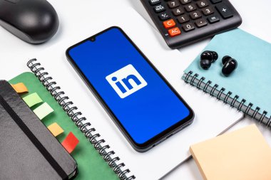 Prag, Çek Cumhuriyeti - 08 18 2025: Merkezde LinkedIn logosunu gösteren bir cep telefonu ile ofis malzemeleri düzenlemesi. LinkedIn, insanları ve şirketleri birbirine bağlayan profesyonel bir ağ..