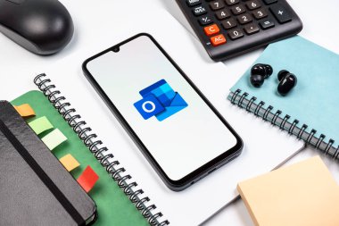 Prag, Çek Cumhuriyeti - 08 18 2025: Merkezde Outlook logosunu gösteren bir cep telefonu ile ofis malzemeleri düzenlemesi. Outlook iletileri göndermek ve yönetmek için bir e- posta platformudur.
