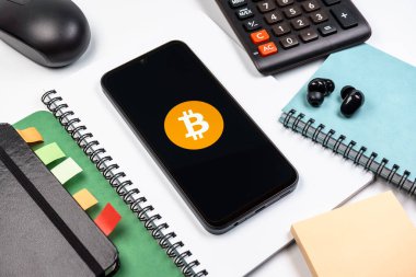Prag, Çek Cumhuriyeti - 08 18 2025: Merkezde Bitcoin logosu sergilenen bir cep telefonu ile ofis malzemeleri düzenlemesi. Bitcoin merkezi olmayan işlemler için dijital bir kripto para birimidir.