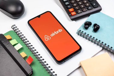 Prag, Çek Cumhuriyeti - 08 18 2025: Merkezde Airbnb logosu sergilenen bir cep telefonu ile ofis malzemeleri düzenlemesi. Airbnb dünya çapında kısa vadeli konaklama için bir platformdur..