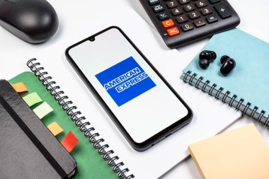 Prag, Çek Cumhuriyeti - 08 18 2025: Merkezde American Express logosunu gösteren bir cep telefonu ile ofis malzemeleri düzenlemesi. American Express kart ve bankacılık sunan bir finans şirketidir..