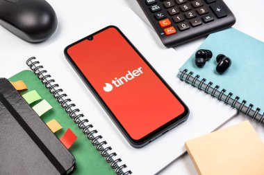 Prag, Çek Cumhuriyeti - 08 18 2025: Merkezde Tinder logosu sergilenen bir cep telefonu ile ofis malzemeleri düzenlemesi. Tinder insanları eşleştirmek ve bağlamak için bir randevu uygulaması.