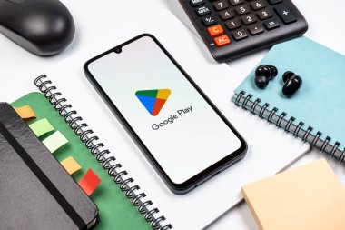 Prag, Çek Cumhuriyeti - 08 18 2025: Merkezde Google Play logosunu gösteren bir cep telefonu ile ofis malzemeleri düzenlemesi. Google Play uygulamaları, oyunları ve dijital içeriği indirmek için bir platformdur.