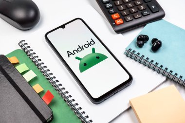 Prag, Çek Cumhuriyeti - 08 18 2025: Merkezde Android logosunu gösteren bir cep telefonu ile ofis malzemeleri düzenlemesi. Android akıllı telefonlar ve tabletler için mobil bir işletim sistemidir..