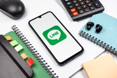 Prag, Çek Cumhuriyeti - 08 18 2025: Merkezinde hat logosu sergilenen bir cep telefonu ile ofis malzemeleri düzenlemesi. Line aramalar, mesajlar ve çokluortam paylaşımı için bir mesajlaşma uygulamasıdır.