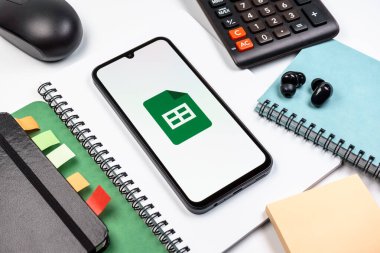 Prag, Çek Cumhuriyeti - 08 18 2025: Merkezde Google Sheets logosunu gösteren bir cep telefonu ile ofis malzemeleri düzenlemesi. Google Sayfalar tablo oluşturmak ve yönetmek için bir platformdur.