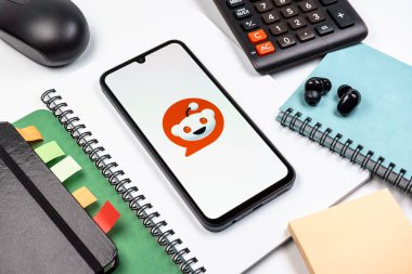 Prag, Çek Cumhuriyeti - 08 18 2025: Merkezde Reddit logosunu gösteren bir cep telefonu ile ofis malzemeleri düzenlemesi. Reddit tartışma, haber ve toplum içeriği için bir platformdur.