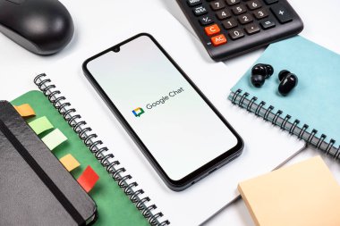 Prag, Çek Cumhuriyeti - 08 18 2025: Merkezde Google Chat logosunu gösteren bir cep telefonu ile ofis malzemeleri düzenlemesi. Google Chat mesajlaşma ve takım işbirliği için bir platformdur.