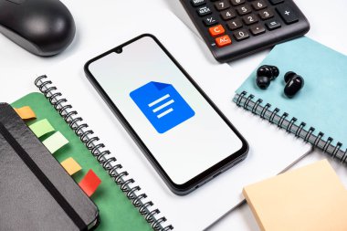 Prag, Çek Cumhuriyeti - 08 18 2025: Merkezde Google Docs logosunu gösteren bir cep telefonu ile ofis malzemeleri düzenlemesi. Google Docs metin belgeleri oluşturmak ve düzenlemek için bir platformdur.