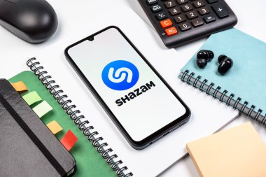 Prag, Çek Cumhuriyeti - 08 18 2025: Merkezinde Shazam logosu bulunan bir cep telefonu ile ofis malzemeleri düzenlemesi. Shazam şarkıları ve müzik parçalarını tanımlamak için bir uygulamadır.