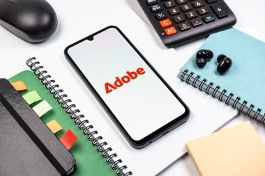 Prag, Çek Cumhuriyeti - 08 18 2025: Merkezde Adobe logosunu gösteren bir cep telefonu ile ofis malzemeleri düzenlemesi. Adobe yaratıcı araçlar ve hizmetler sunan bir yazılım şirketidir..
