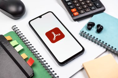 Prag, Çek Cumhuriyeti - 08 18 2025: Merkezinde Acrobat Reader logosu bulunan bir cep telefonu ile ofis malzemeleri düzenlemesi. Acrobat Reader, PDF belgelerini görüntülemek ve yönetmek için bir platformdur.