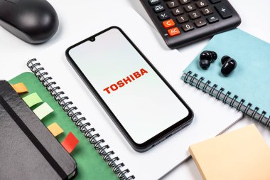 Prag, Çek Cumhuriyeti - 08 18 2025: Merkezde Toshiba logosunu gösteren bir cep telefonu ile ofis malzemeleri düzenlemesi. Toshiba elektronik ve cihaz üreten bir teknoloji şirketidir..