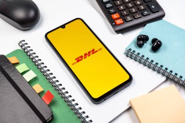 Prag, Çek Cumhuriyeti - 08 18 2025: Merkezde DHL logosu sergilenen bir cep telefonu ile ofis malzemeleri düzenlemesi. DHL uluslararası nakliye hizmeti sunan bir lojistik şirketidir..