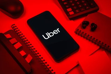 Prag, Çek Cumhuriyeti - 08 18 2025: Merkezde Uber logosu gösteren bir cep telefonu ile ofis malzemeleri düzenlemesi. Uber ulaşım ve dağıtım hizmetleri için bir gezinti selamlama uygulaması.