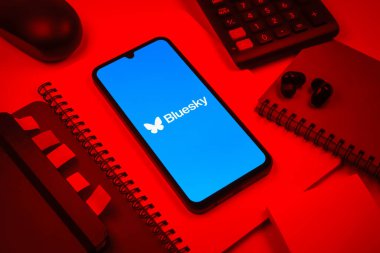 Prag, Çek Cumhuriyeti - 08 18 2025: Merkezde Bluesky logosunu gösteren bir cep telefonu ile ofis malzemeleri düzenlemesi. Bluesky merkezi olmayan ağlar için bir sosyal medya platformudur..