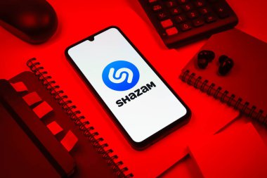 Prag, Çek Cumhuriyeti - 08 18 2025: Merkezinde Shazam logosu bulunan bir cep telefonu ile ofis malzemeleri düzenlemesi. Shazam şarkıları ve müzik parçalarını tanımlamak için bir uygulamadır.