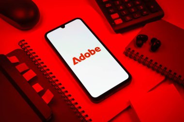Prag, Çek Cumhuriyeti - 08 18 2025: Merkezde Adobe logosunu gösteren bir cep telefonu ile ofis malzemeleri düzenlemesi. Adobe yaratıcı araçlar ve hizmetler sunan bir yazılım şirketidir..