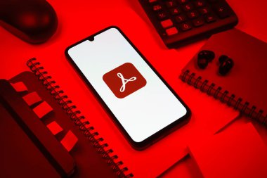 Prag, Çek Cumhuriyeti - 08 18 2025: Merkezinde Acrobat Reader logosu bulunan bir cep telefonu ile ofis malzemeleri düzenlemesi. Acrobat Reader, PDF belgelerini görüntülemek ve yönetmek için bir platformdur.