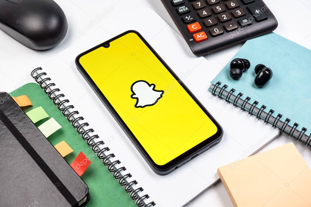 Prague, Czechia - 08 18 2025: An arrangement of office supplies with a mobile phone in the center displaying Snapchat logo. Snapchat is an app for sending photos, videos, and temporary messages.