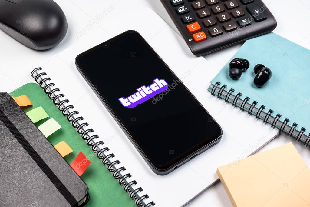 Prague, Czechia - 08 18 2025: An arrangement of office supplies with a mobile phone in the center displaying Twitch logo. Twitch is a platform for live streaming games and content.