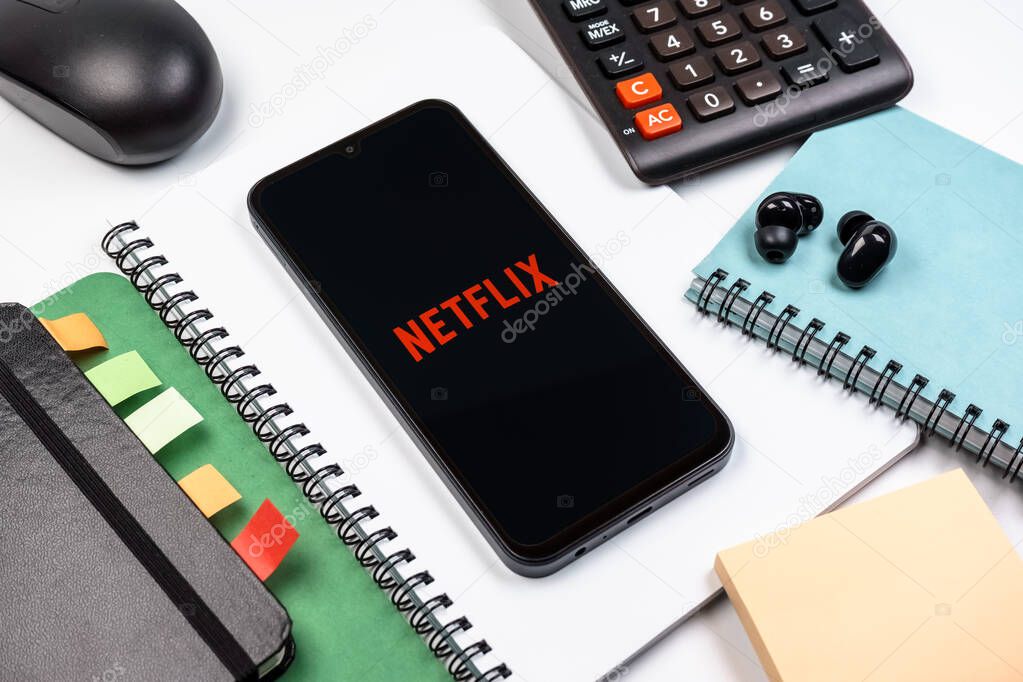 Prague, Czechia - 08 18 2025: An arrangement of office supplies with a mobile phone in the center displaying Netflix logo. Netflix is a streaming platform for movies and TV shows.