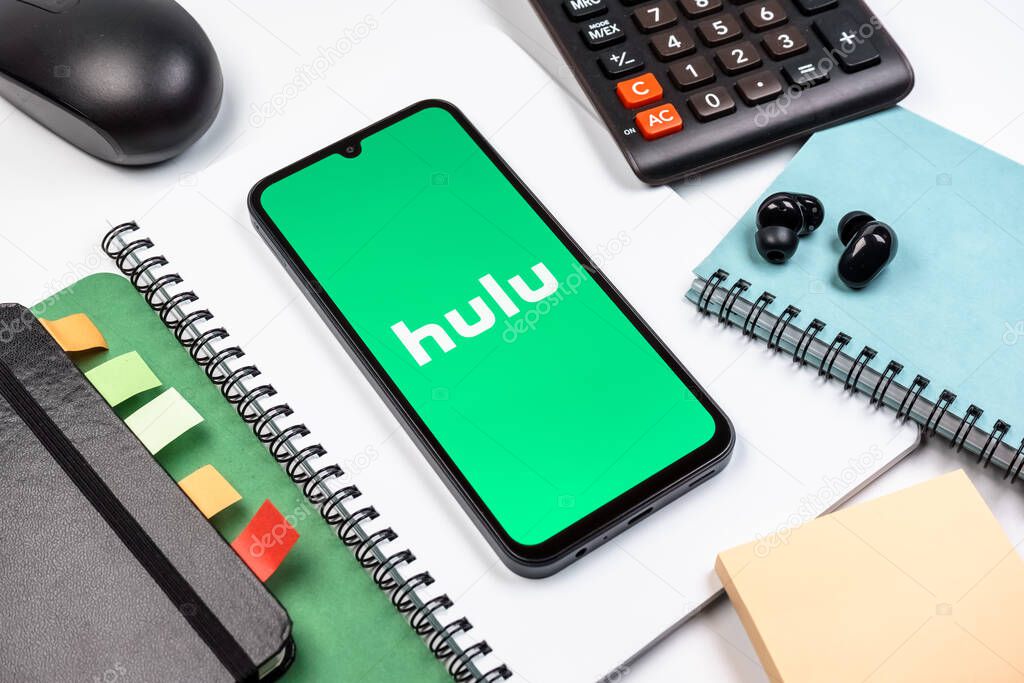 Prague, Czechia - 08 18 2025: An arrangement of office supplies with a mobile phone in the center displaying Hulu logo. Hulu is a streaming platform for TV shows, movies, and live TV.