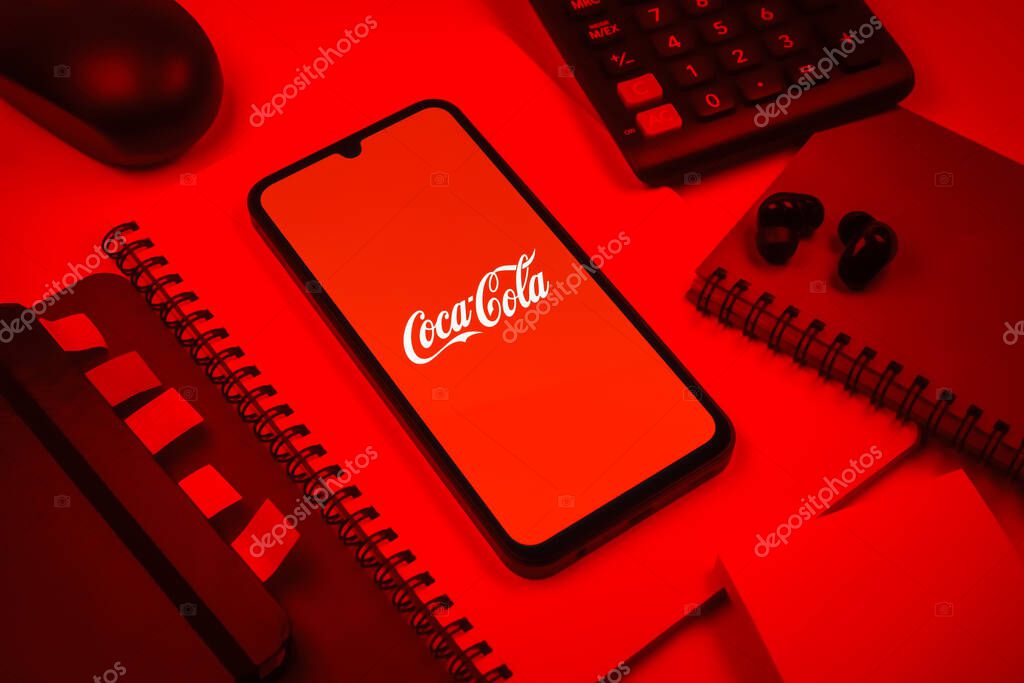 Prague, Czechia - 08 18 2025: An arrangement of office supplies with a mobile phone in the center displaying Coca-Cola logo. Coca-Cola is a beverage company known for its soft drinks.