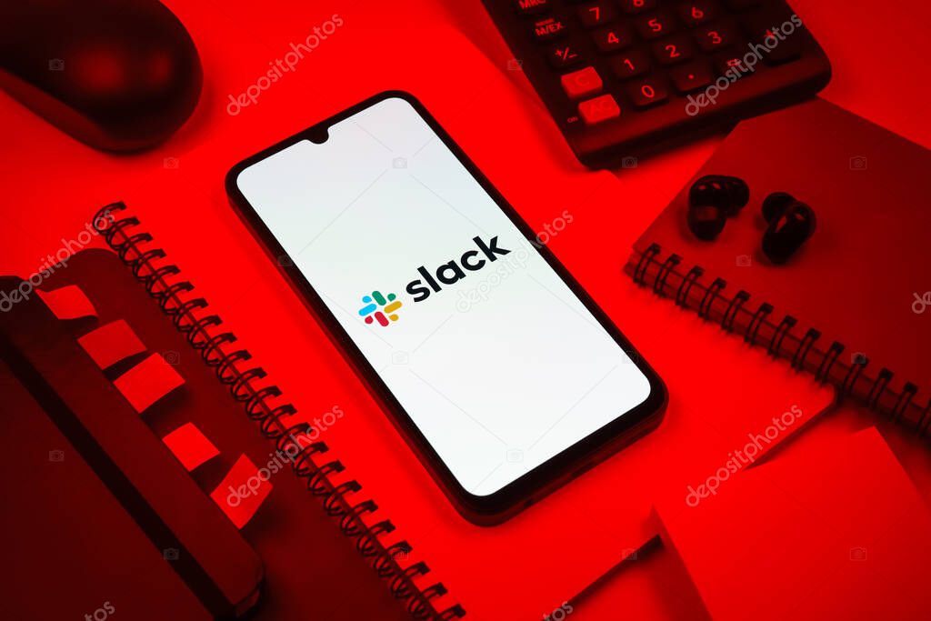 Prague, Czechia - 08 18 2025: An arrangement of office supplies with a mobile phone in the center displaying Slack logo. Slack is a platform for team messaging and workplace communication.