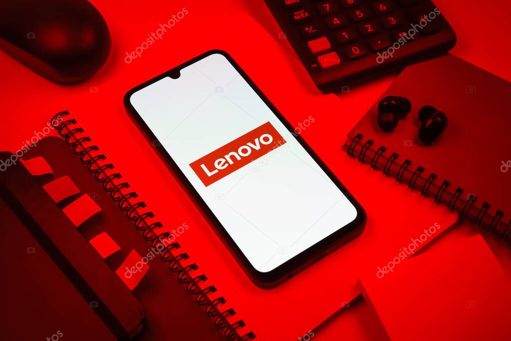 Prague, Czechia - 08 18 2025: An arrangement of office supplies with a mobile phone in the center displaying Lenovo logo. Lenovo is a technology company producing computers and electronics.