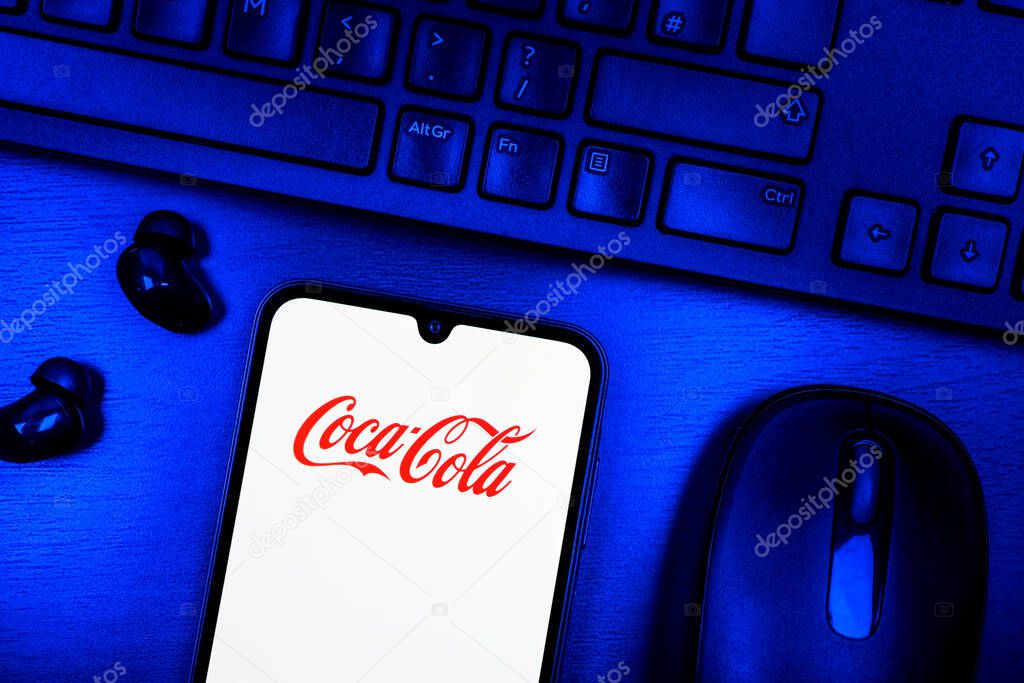 Prague, Czechia - 08 09 2025: A top-down view of a desk with a phone displaying the Coca-Cola logo. Coca-Cola is a beverage company known for its soft drinks.