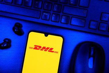 Prague, Czechia - 08 09 2025: A top-down view of a desk with a phone displaying the DHL logo. DHL is a logistics company offering international shipping services.