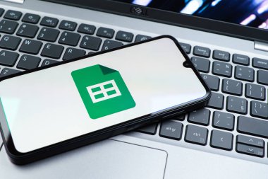 Prag, Çek Cumhuriyeti - 08 01 2025: Laptop klavyesinde duran bir cep telefonu Google Sheets logosunu görüntüler. Google Sayfalar tablo oluşturmak ve yönetmek için bir platformdur.