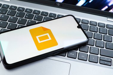Prag, Çek Cumhuriyeti - 08 01 2025: Laptop klavyesinde duran bir cep telefonu Google Slides logosunu görüntüler. Google Slides sunumlar ve slayt gösterileri oluşturmak için bir platformdur.