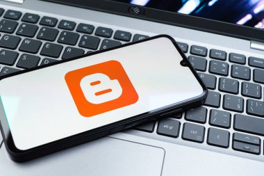 Prag, Çek Cumhuriyeti - 08 01 2025: Dizüstü bilgisayarın üzerinde duran bir cep telefonu Blogger logosunu gösterir. Blogger blog oluşturma ve yayınlama için bir platformdur.