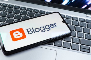 Prag, Çek Cumhuriyeti - 08 01 2025: Dizüstü bilgisayarın üzerinde duran bir cep telefonu Blogger logosunu gösterir. Blogger blog oluşturma ve yayınlama için bir platformdur.