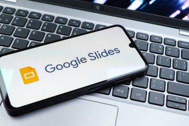 Prag, Çek Cumhuriyeti - 08 01 2025: Laptop klavyesinde duran bir cep telefonu Google Slides logosunu görüntüler. Google Slides sunumlar ve slayt gösterileri oluşturmak için bir platformdur.