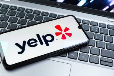 Prag, Çek Cumhuriyeti - 08 01 2025: Laptop klavyesinde duran bir cep telefonu Yelp logosunu gösterir. Yelp yerel işletmeleri bulmak ve incelemek için bir platformdur.