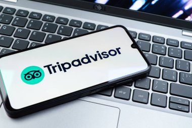Prag, Çek Cumhuriyeti - 08 01 2025: Dizüstü bilgisayarın üzerinde bulunan bir cep telefonu TripDanışman logosunu gösteriyor. Seyahat danışmanı seyahat değerlendirmeleri, rezervasyonlar ve tavsiyeler için bir platformdur..