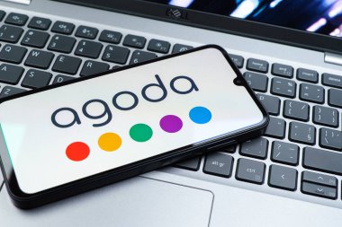 Prag, Çek Cumhuriyeti - 08 01 2025: Dizüstü bilgisayarın üzerinde duran bir cep telefonu Agoda logosunu gösteriyor. Agoda, otelleri ve seyahat yerlerini ayırtmak için bir platform..